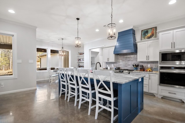 kitchen with appliances with stainless steel finishes, pendant lighting, white cabinetry, custom range hood, and a center island with sink