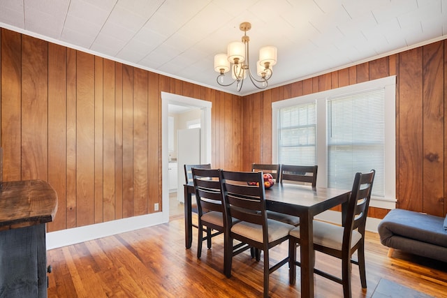 dining room with an inviting chandelier, wood-type flooring, and wooden walls