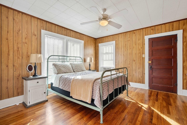 bedroom featuring crown molding, ceiling fan, wood-type flooring, and wood walls