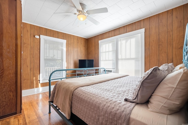 bedroom featuring multiple windows, hardwood / wood-style floors, wooden walls, and ceiling fan