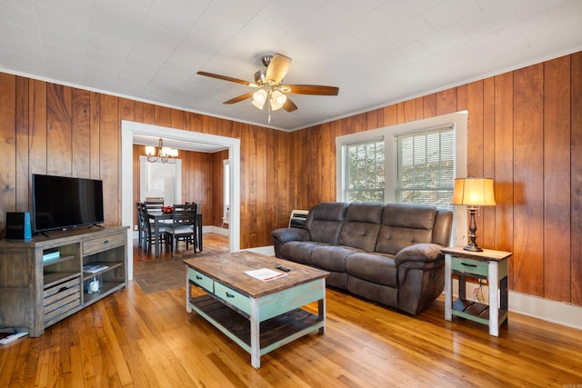 living room featuring ornamental molding, wooden walls, ceiling fan with notable chandelier, and light wood-type flooring