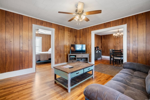 living room featuring crown molding, hardwood / wood-style floors, ceiling fan with notable chandelier, and wooden walls