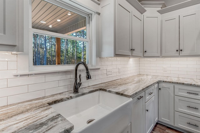 kitchen with white cabinetry, sink, tasteful backsplash, and light stone countertops