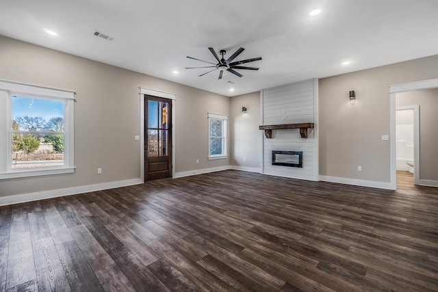 unfurnished living room featuring ceiling fan, a large fireplace, dark hardwood / wood-style flooring, and a wealth of natural light