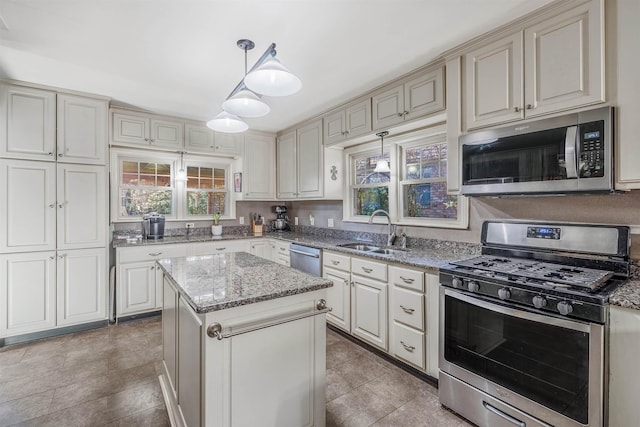 kitchen featuring sink, stone counters, stainless steel appliances, a center island, and decorative light fixtures