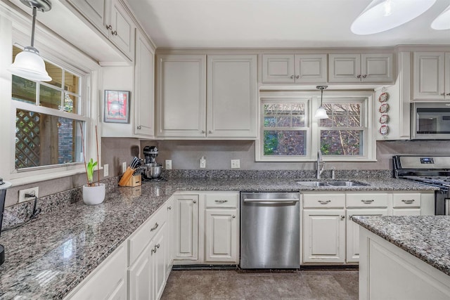 kitchen featuring dark stone countertops, sink, stainless steel appliances, and hanging light fixtures