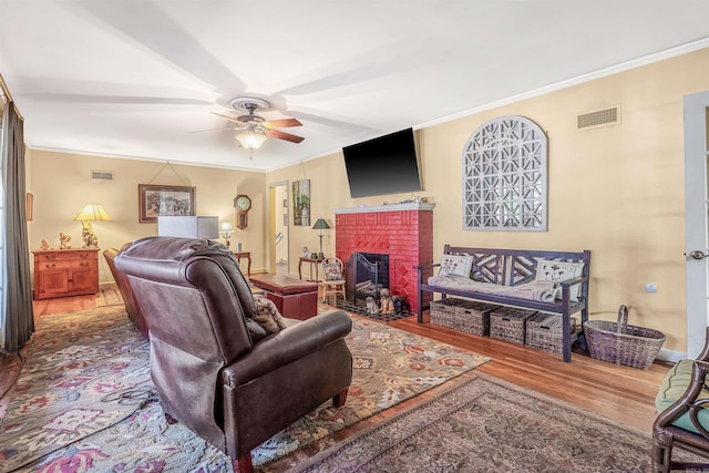 living room featuring hardwood / wood-style floors, crown molding, a fireplace, and ceiling fan