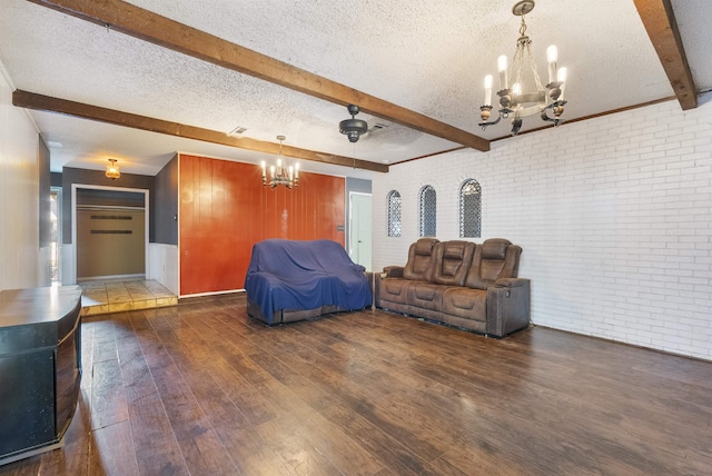 unfurnished living room featuring dark wood-type flooring, a textured ceiling, brick wall, ceiling fan with notable chandelier, and beamed ceiling