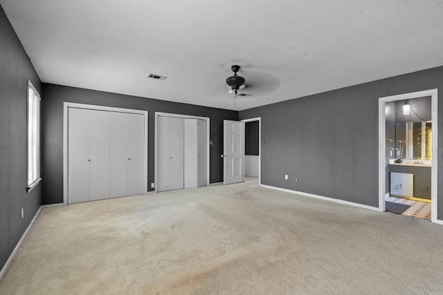 unfurnished bedroom featuring multiple closets, ceiling fan, light carpet, and ensuite bath