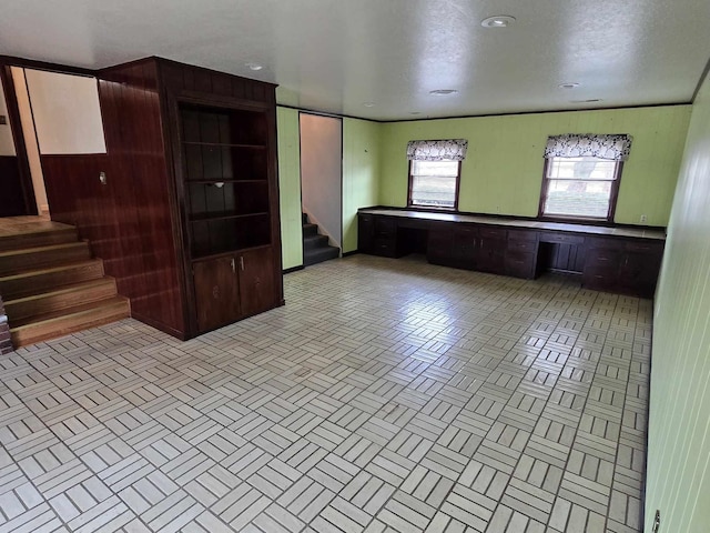 unfurnished living room featuring built in desk, a textured ceiling, and wooden walls