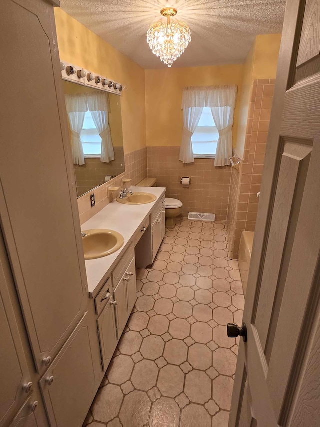 bathroom featuring a notable chandelier, vanity, a textured ceiling, and tile walls