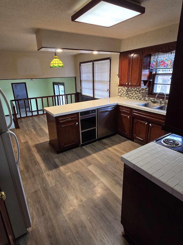 kitchen featuring refrigerator, wood-type flooring, sink, stainless steel dishwasher, and kitchen peninsula