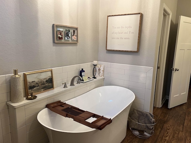 bathroom with hardwood / wood-style flooring, a bath, and tile walls