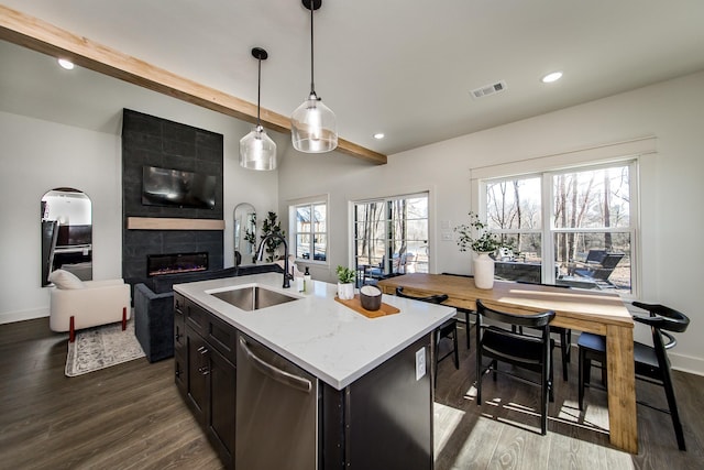 kitchen featuring sink, hanging light fixtures, stainless steel dishwasher, a tile fireplace, and a kitchen island with sink