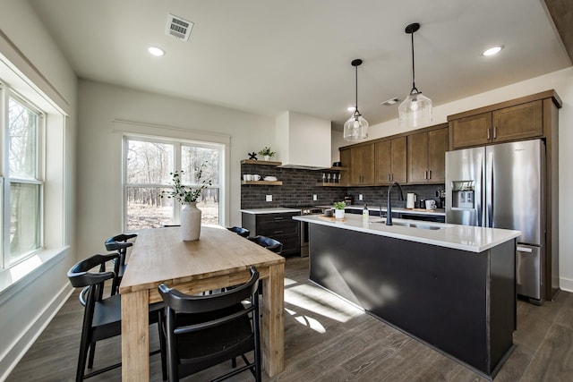 kitchen with sink, an island with sink, pendant lighting, stainless steel appliances, and wall chimney range hood