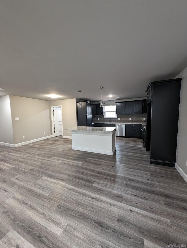 kitchen featuring hanging light fixtures, a center island, stainless steel dishwasher, light stone counters, and dark wood-type flooring