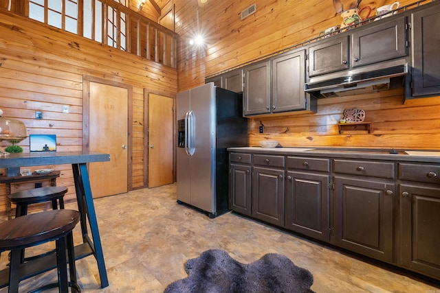 kitchen with dark brown cabinetry, stainless steel fridge, and wooden walls