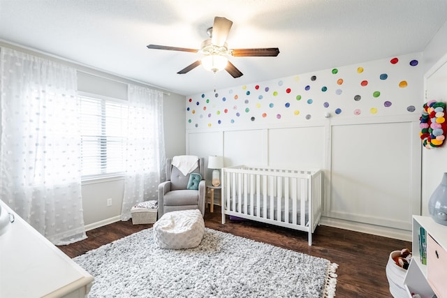 bedroom with ceiling fan, dark hardwood / wood-style floors, and a crib