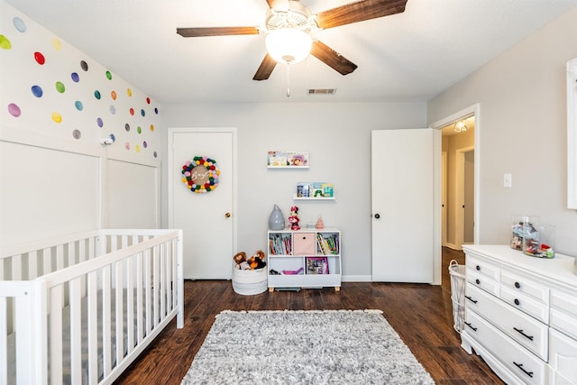 bedroom featuring a nursery area, dark hardwood / wood-style floors, and ceiling fan