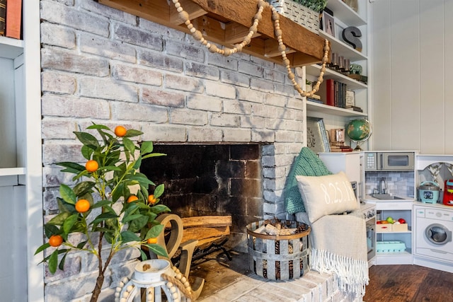 living area with dark hardwood / wood-style flooring, sink, washer / dryer, and a brick fireplace