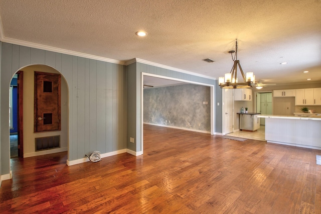 unfurnished living room featuring a textured ceiling, ornamental molding, hardwood / wood-style floors, and a notable chandelier