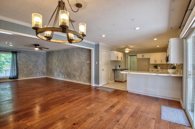 kitchen with light wood-type flooring, kitchen peninsula, white cabinets, hanging light fixtures, and ornamental molding