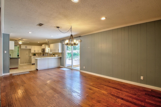 unfurnished living room featuring light hardwood / wood-style flooring, hanging light fixtures, crown molding, white cabinetry, and kitchen peninsula