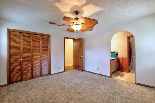 unfurnished bedroom featuring a closet, a textured ceiling, ensuite bathroom, ceiling fan, and light colored carpet