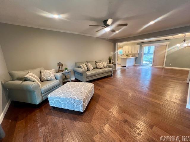 living room featuring dark hardwood / wood-style flooring, crown molding, and ceiling fan with notable chandelier