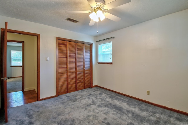 unfurnished bedroom with a textured ceiling, a closet, dark carpet, and ceiling fan