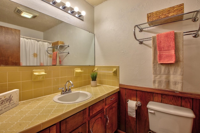 bathroom featuring wooden walls, vanity, toilet, and backsplash