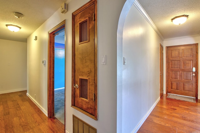 hall with a textured ceiling, crown molding, and light hardwood / wood-style flooring