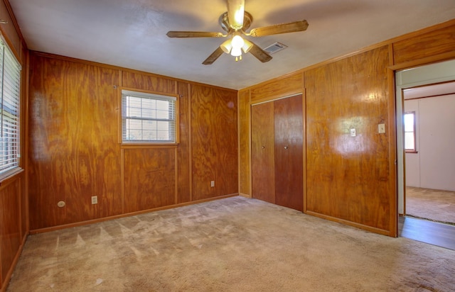 unfurnished bedroom featuring light colored carpet, ceiling fan, and wood walls