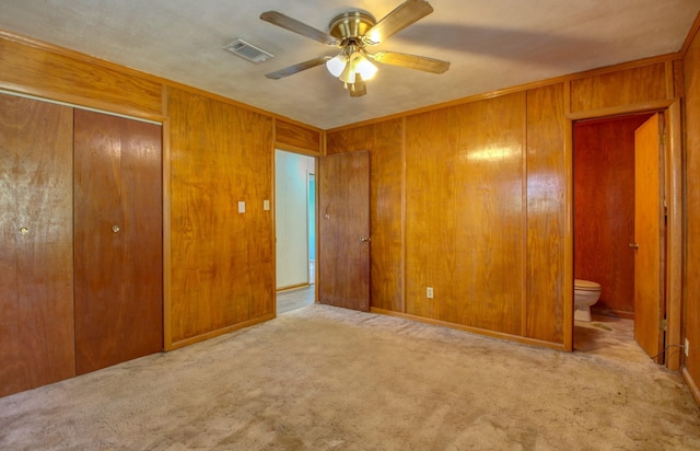 unfurnished bedroom with a closet, wooden walls, ensuite bath, and light carpet