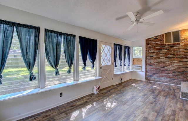 unfurnished room with brick wall, lofted ceiling, a textured ceiling, and dark hardwood / wood-style flooring