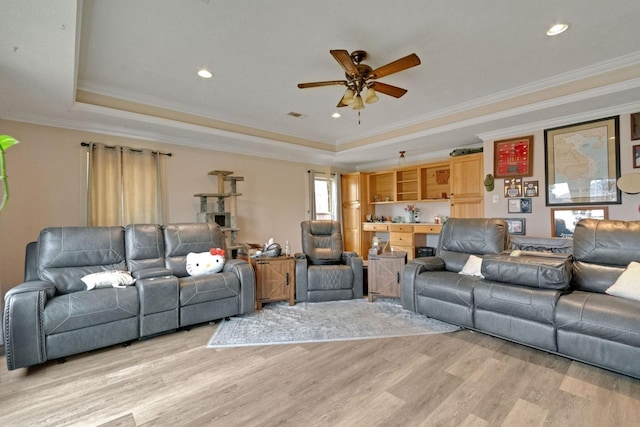 living room with ceiling fan, ornamental molding, a tray ceiling, and light hardwood / wood-style flooring