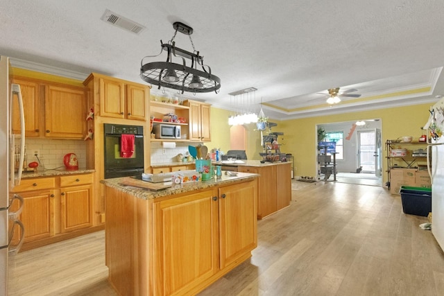 kitchen with appliances with stainless steel finishes, hanging light fixtures, light hardwood / wood-style floors, a kitchen island, and a raised ceiling