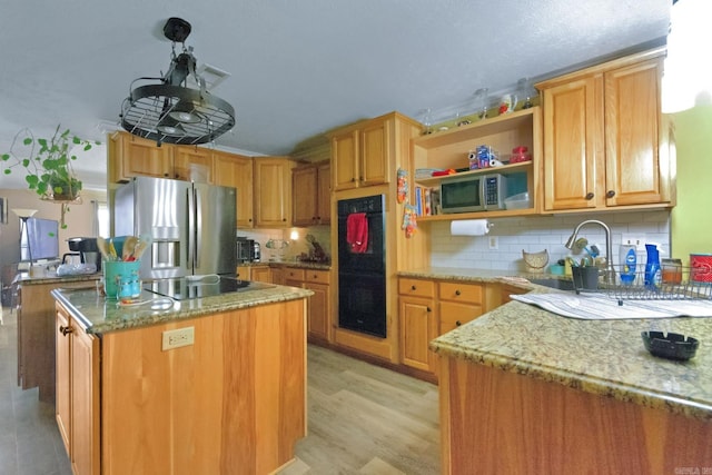 kitchen with light hardwood / wood-style flooring, backsplash, a center island, light stone counters, and black appliances