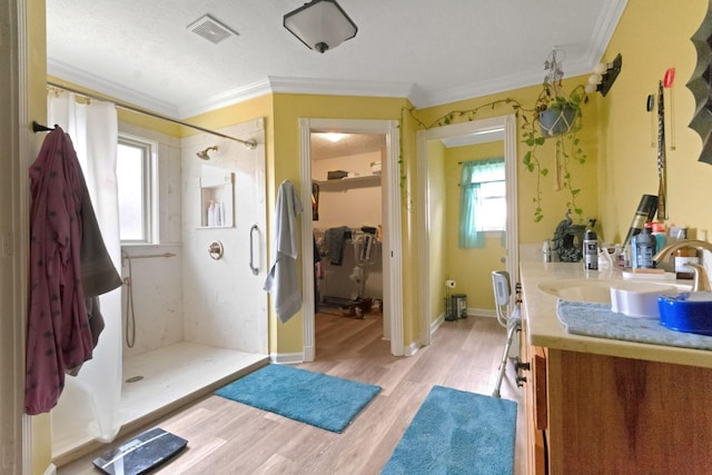 bathroom featuring hardwood / wood-style flooring, vanity, ornamental molding, and walk in shower