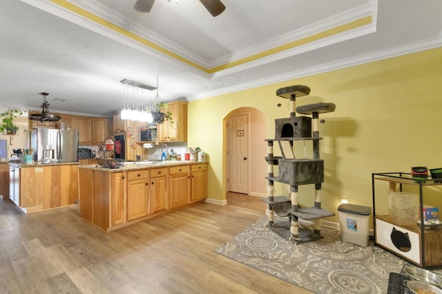 kitchen featuring crown molding, light wood-type flooring, appliances with stainless steel finishes, a raised ceiling, and pendant lighting