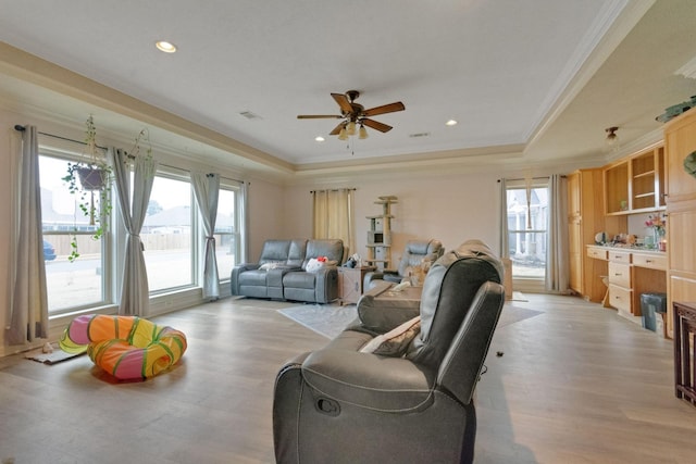 living room featuring ornamental molding, ceiling fan, light wood-type flooring, and a tray ceiling