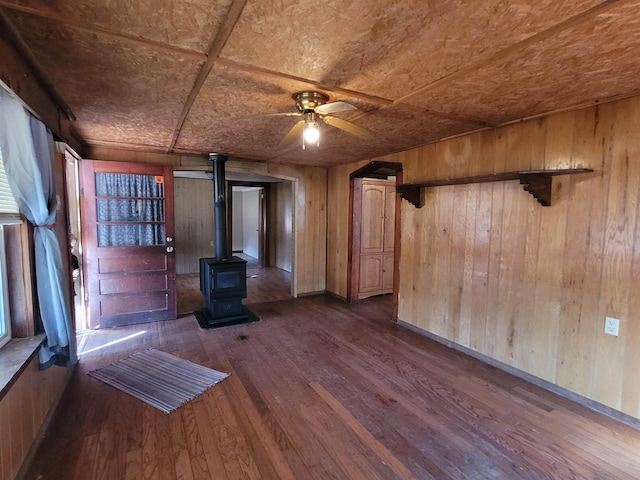 interior space featuring ceiling fan, a wood stove, wooden walls, and dark hardwood / wood-style floors