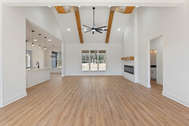 unfurnished living room with sink, ceiling fan, beam ceiling, a large fireplace, and light wood-type flooring