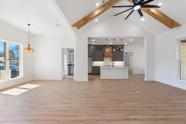 unfurnished living room with sink, high vaulted ceiling, light hardwood / wood-style flooring, beamed ceiling, and ceiling fan