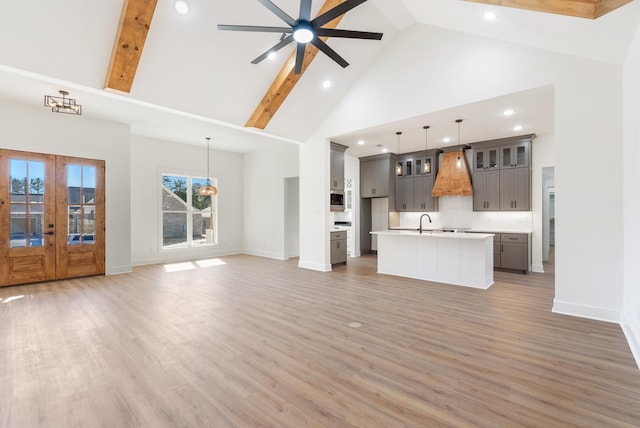 unfurnished living room with sink, dark wood-type flooring, ceiling fan with notable chandelier, and high vaulted ceiling