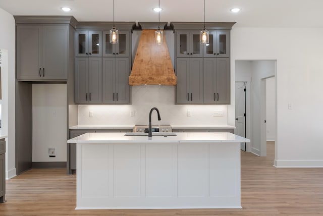 kitchen featuring decorative light fixtures, an island with sink, and custom range hood