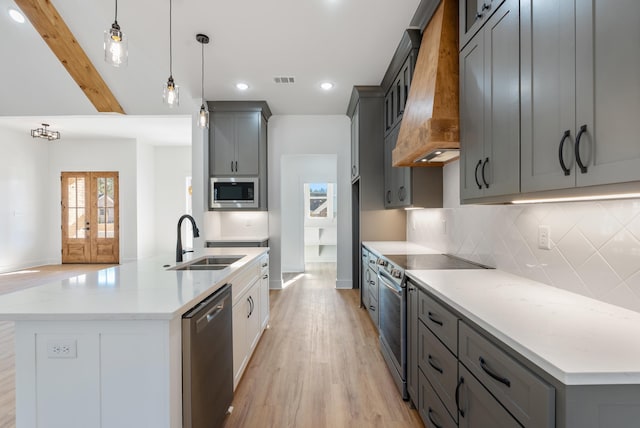 kitchen featuring appliances with stainless steel finishes, sink, hanging light fixtures, custom range hood, and a center island with sink