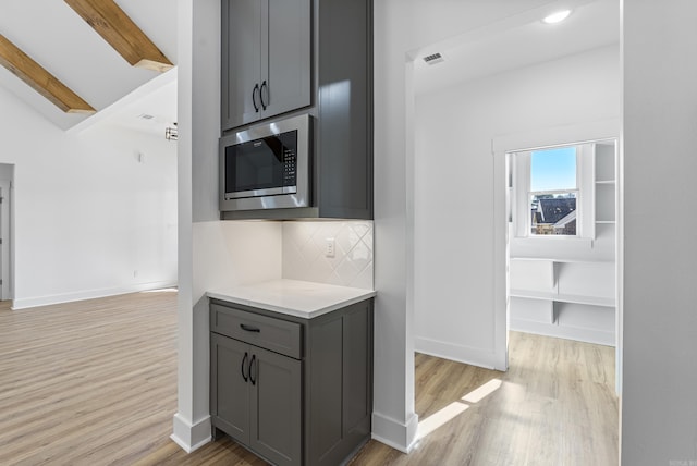 kitchen with gray cabinetry, stainless steel microwave, tasteful backsplash, beamed ceiling, and light wood-type flooring