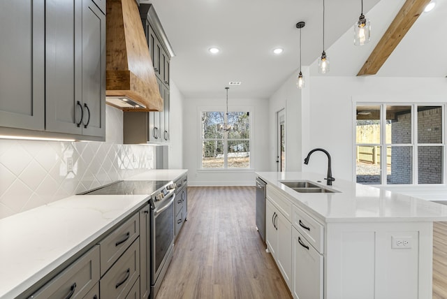 kitchen featuring premium range hood, appliances with stainless steel finishes, pendant lighting, sink, and a center island with sink