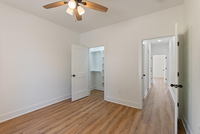 unfurnished bedroom featuring ceiling fan, a spacious closet, a closet, and light wood-type flooring